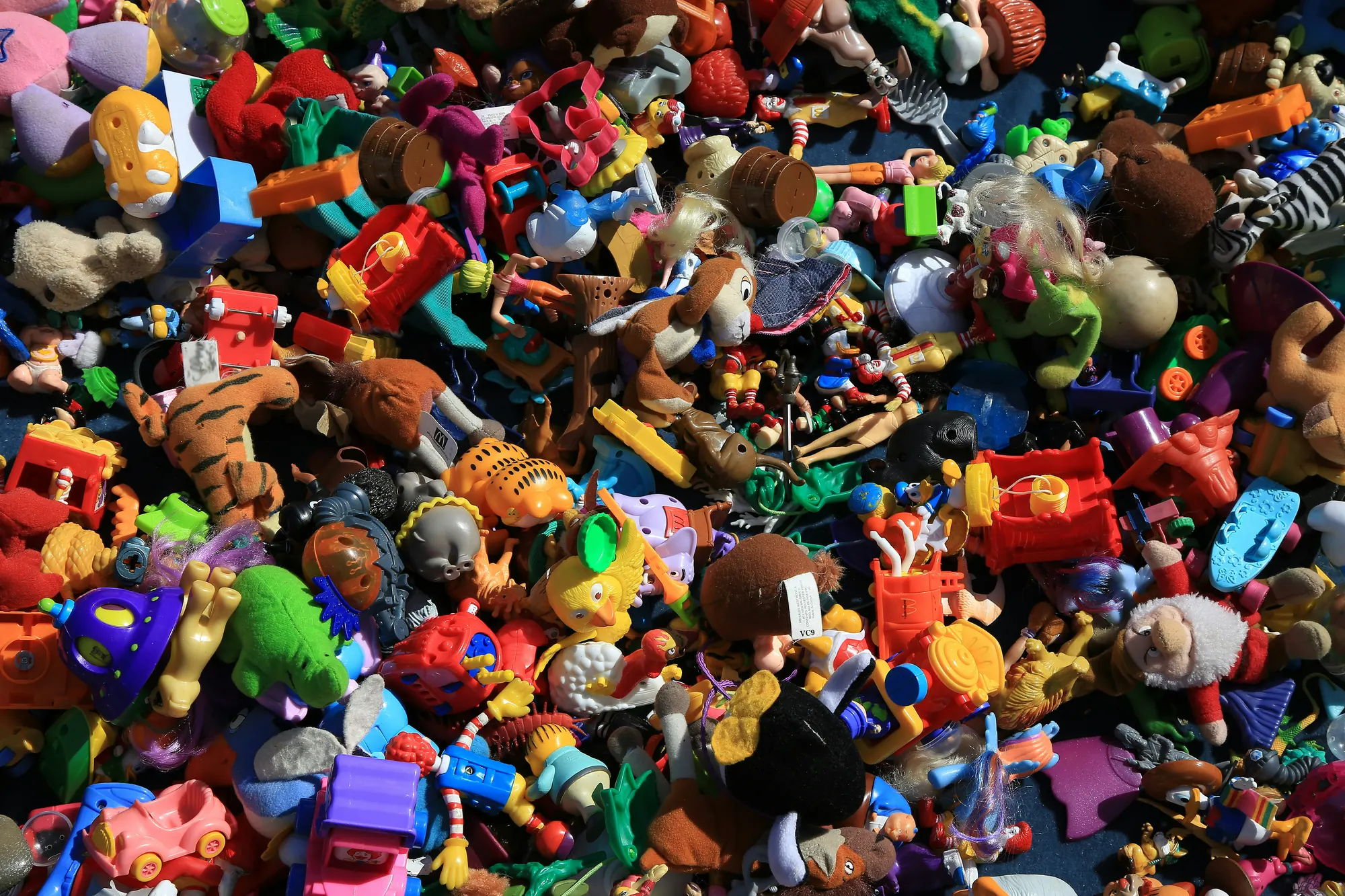 A big jumbled pile of colourful toys — soft toys, figures and plastic vehicles